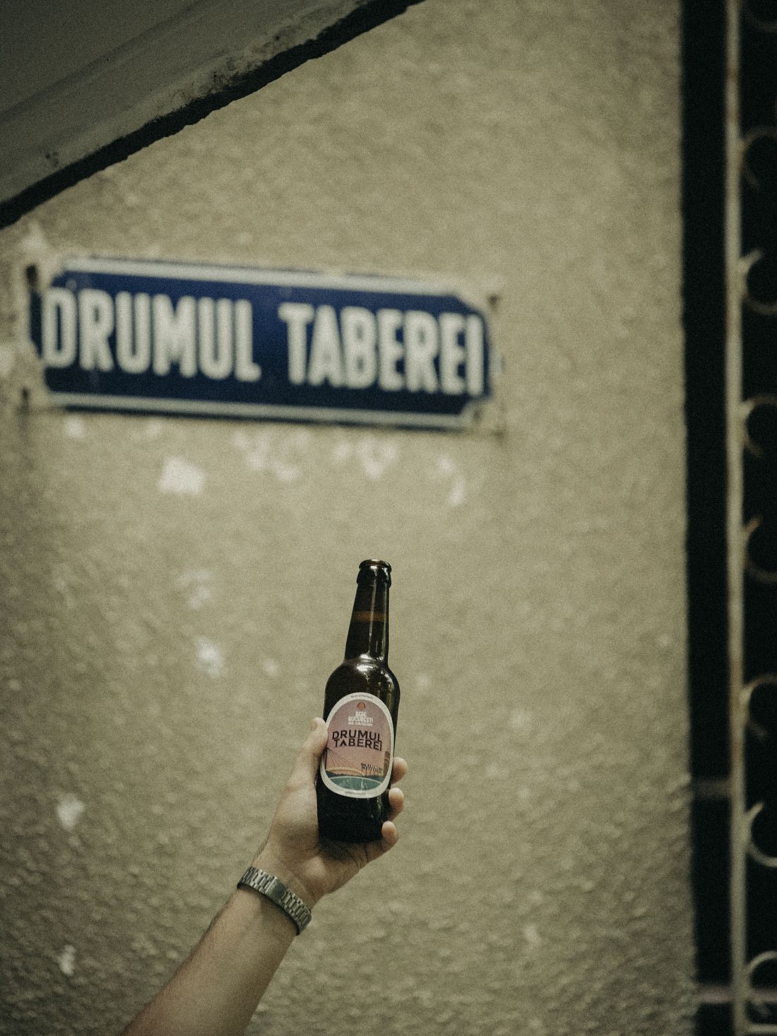 O mână ridică o sticlă sub plăcuța albastră de stradă Drumul Taberei